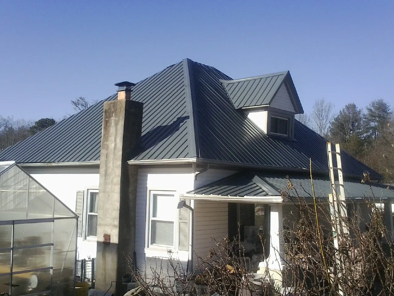 Dark blue standing seam metal roof on a white farmhouse with dormer — Slate & Tile Roof Repair by Roofing Brothers in Conway